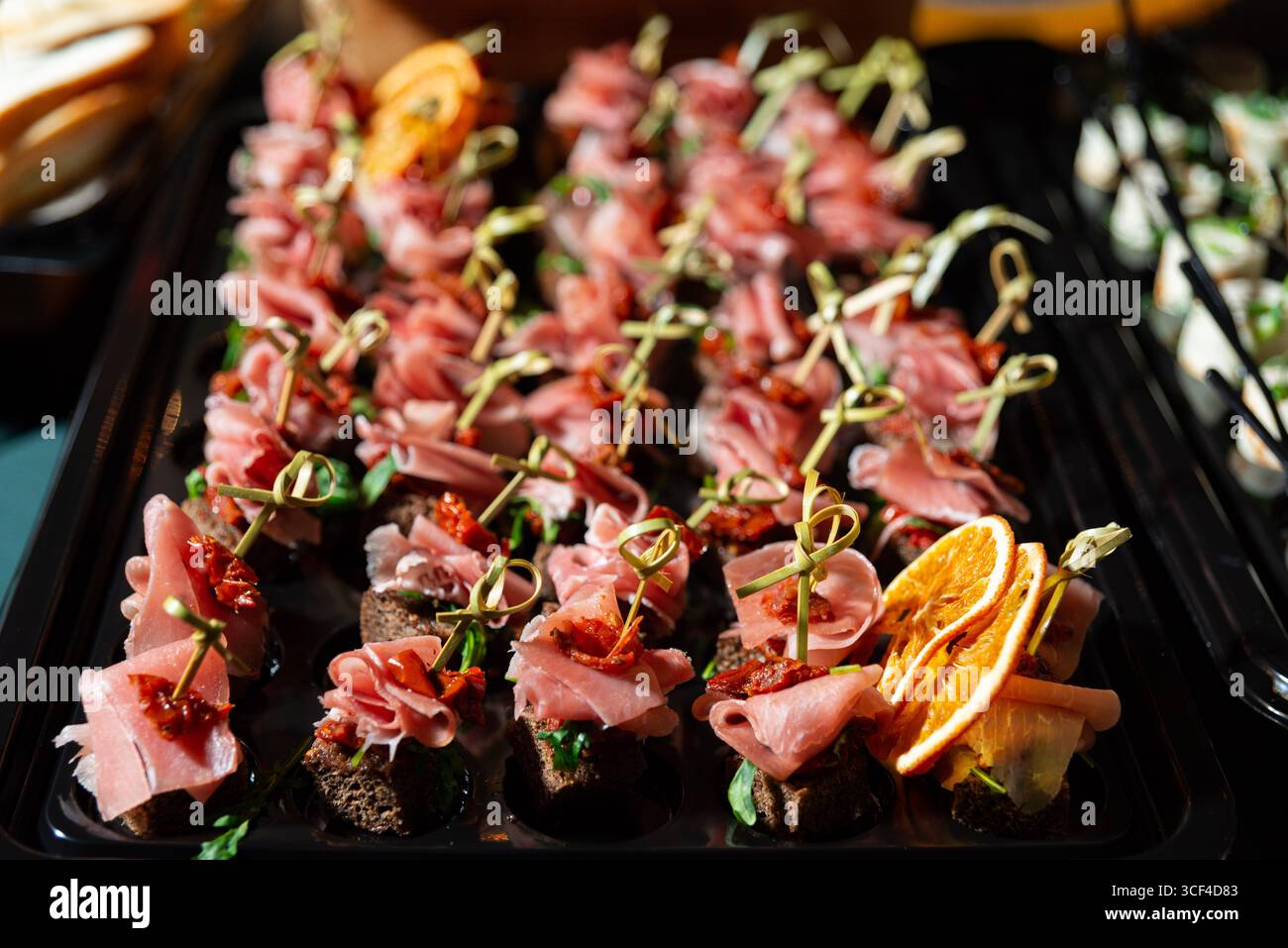 Eine wunderschön angeordnete Platte mit Kanapees mit Wurstwaren, Zitrusscheiben und Kräutern. Perfekt für festliche Feiern oder Veranstaltungen mit Catering, Offerin Stockfoto