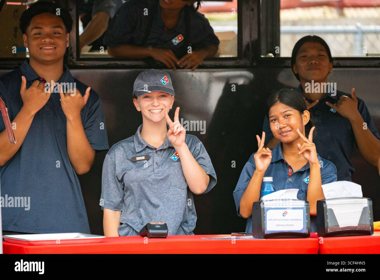 Honolulu, HI USA - 09. November 2024: Mitarbeiter von Domino's Pizza teilen shaka und Frieden, lächeln an einem mobilen Lebensmittelstand für Fußballspiele im Freien Stockfoto