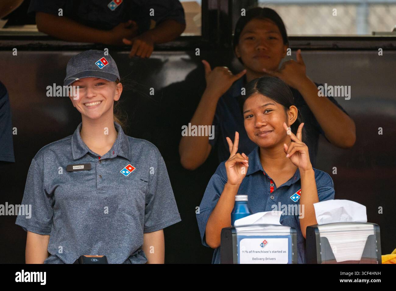 Honolulu, HI USA - 09. November 2024: Mitarbeiter von Domino's Pizza teilen shaka und Frieden, lächeln an einem mobilen Lebensmittelstand für Fußballspiele im Freien Stockfoto