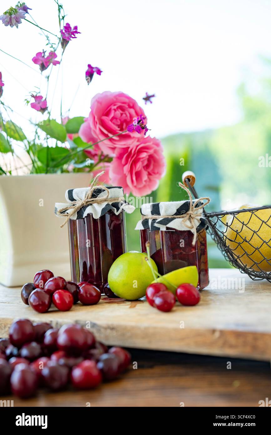 Frische hausgemachte Kirschmarmelade in einem Glas. Zutaten zur Konservierung von Obst auf Holztisch. Vertikale Küchenszene für hausgemachte Küche. Stockfoto Frische hausgemachte Kirschmarmelade in einem Glas. Zutaten zur Konservierung von Obst auf Holztisch. Vertikale Küchenszene für hausgemachte Küche. Stockfoto