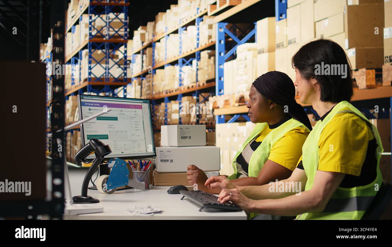 Ein Team aus zwei Mitarbeitern überwacht die Versandroute mit der Sendungssoftware, zeigt auf den pc-Monitor und aktualisiert die Paketversanddetails. Logistische Daten auf dem Computer eingeben. Kamera A.. Stockfoto