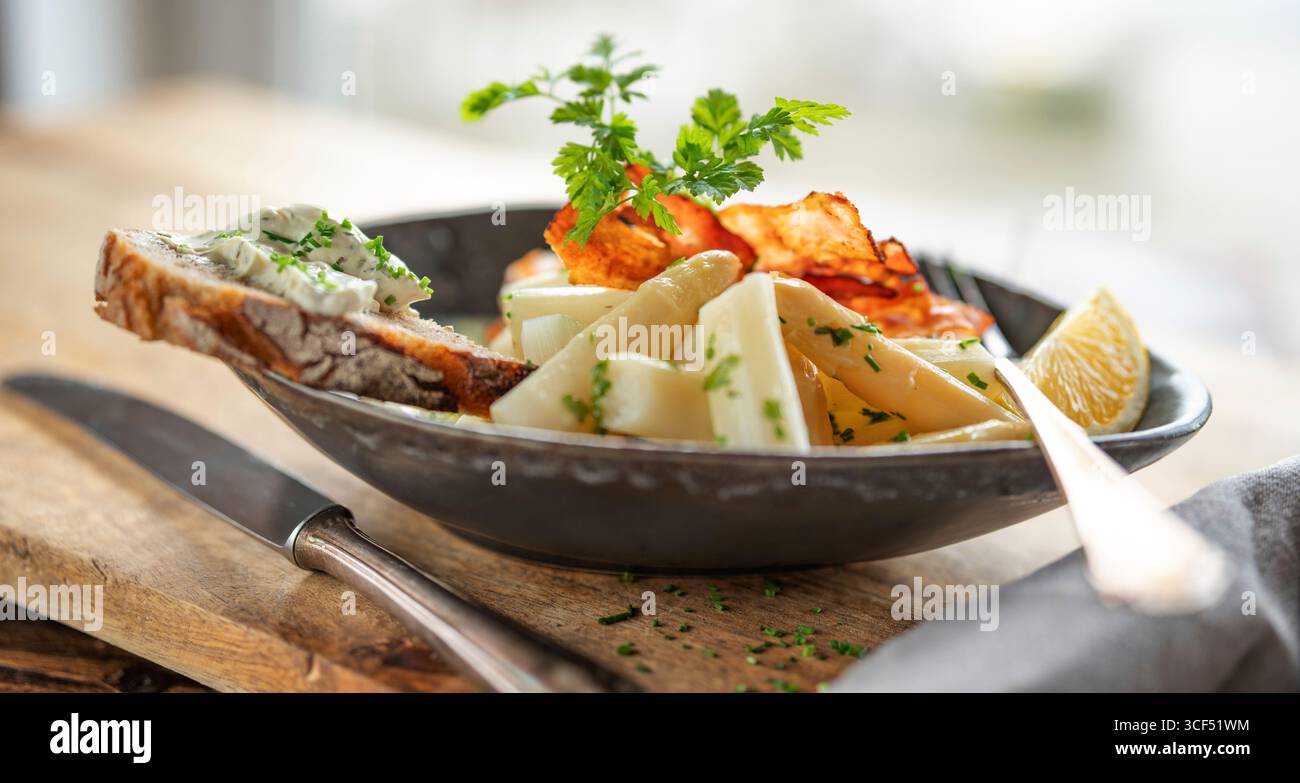 Weißer Spargel mit frischen Zutaten in einer dunklen Keramikschale auf rustikalem Holz. Hintergrund für halthy Nutrion und Fitness. Stockfoto