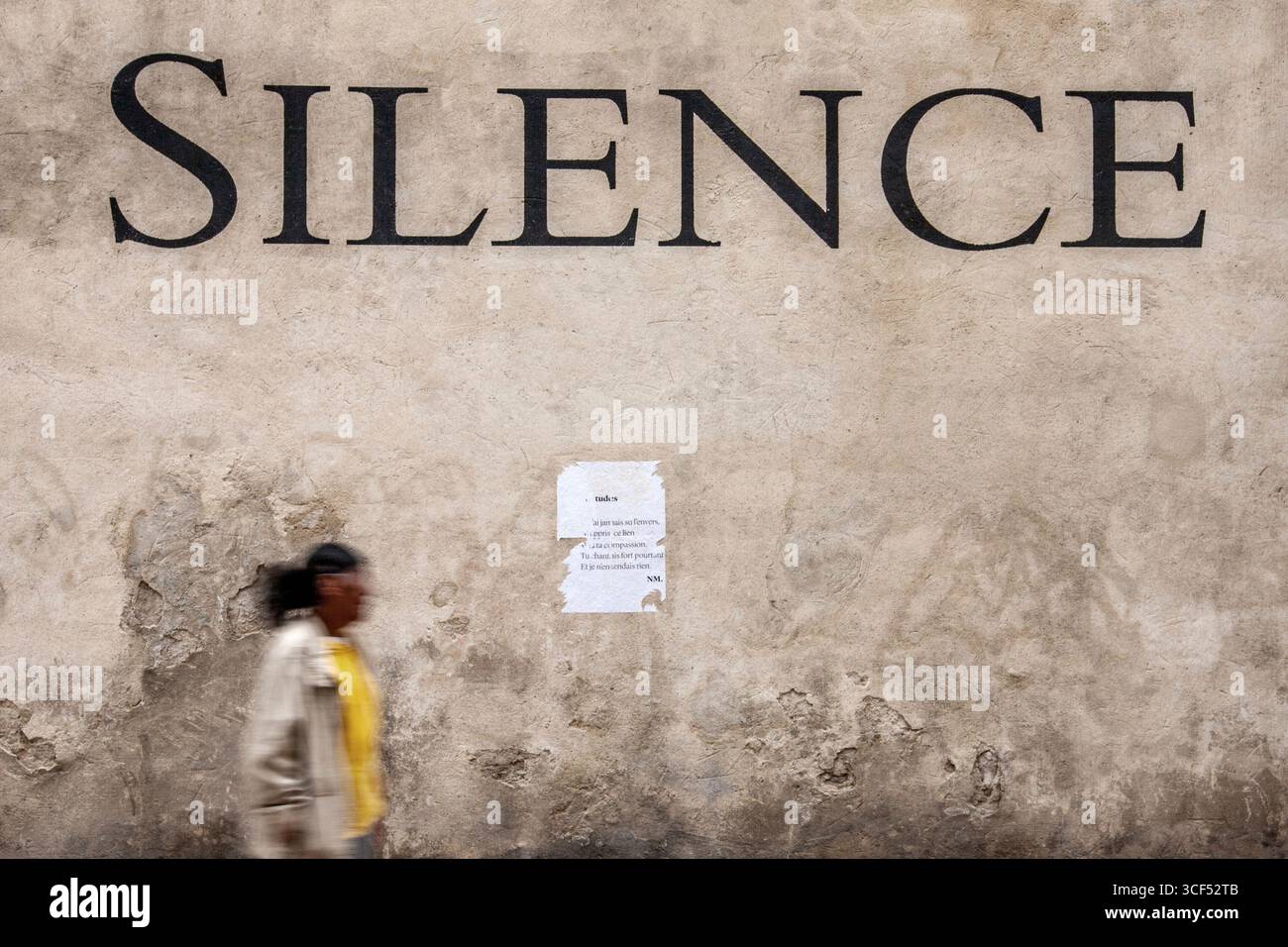 Große Schrift „Silence“ an einer beigefarbenen Wand mit einer Person, die in einer städtischen Umgebung vorbeiläuft Stockfoto