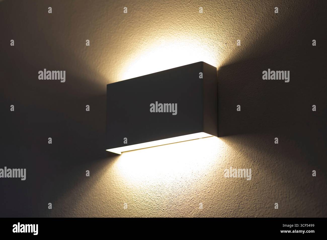 Die moderne Wandleuchte strahlt ein warmes, einladendes Licht aus und strahlt ein sanftes Licht auf die strukturierte Oberfläche der Wand in einem schwach beleuchteten Raum aus, wodurch eine gemütliche und stimmungsvolle Atmosphäre entsteht Stockfoto