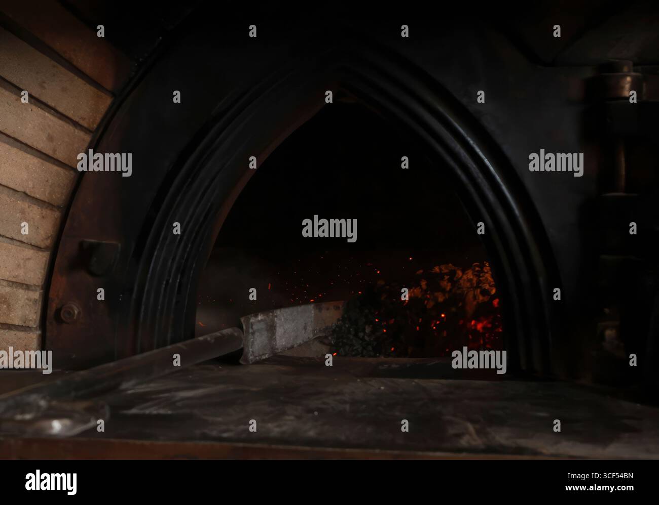 Baker reinigt den Boden eines holzbefeuerten Ofens, glühende Glut beleuchtet das dunkle Interieur und schafft die ideale Umgebung für das Backen von frischem, handwerklichem Brot Stockfoto Baker reinigt den Boden eines holzbefeuerten Ofens, glühende Glut beleuchtet das dunkle Interieur und schafft die ideale Umgebung für das Backen von frischem, handwerklichem Brot Stockfoto