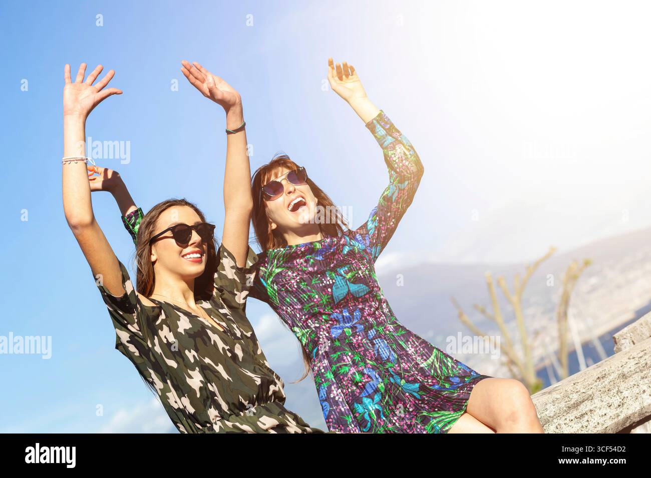Zwei junge Touristen, die eine Sonnenbrille tragen, heben ihre Arme vor Freude und genießen die Sonne in Neapel, während sich der berühmte Vesuv majestätisch im Hintergrund erhebt Stockfoto