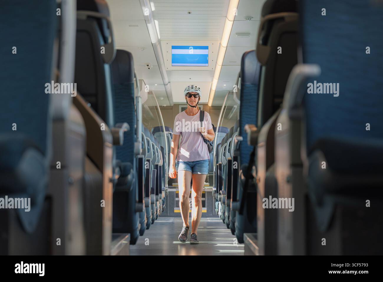 Eine Frau mit Helm schlendert an einem sonnigen Tag durch einen geräumigen Zug mit bequemen Sitzgelegenheiten und geht möglicherweise zu einem Outdoor-Abenteuer. Stockfoto