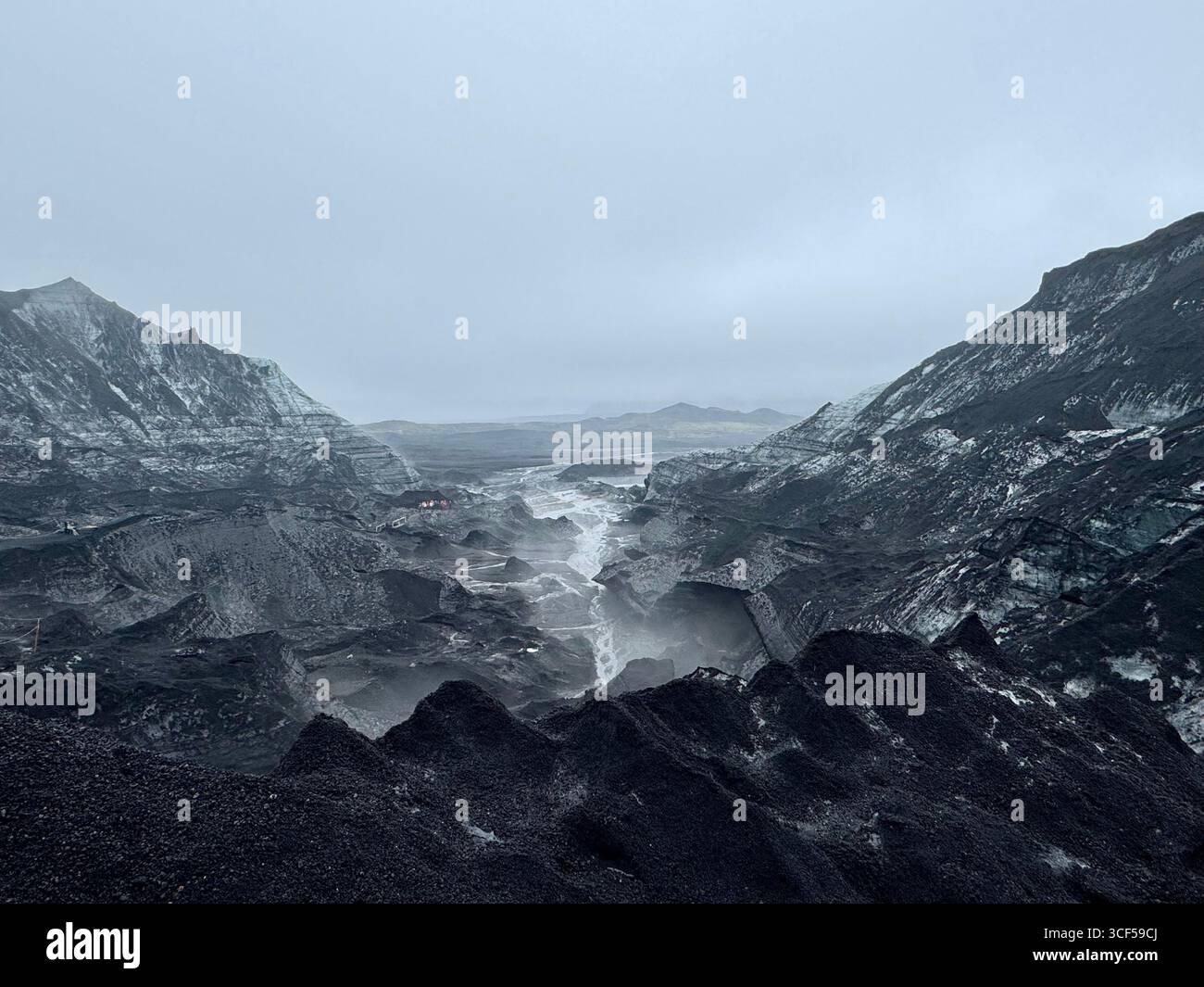 Gletscherabfluss zwischen Hügeln, die aus Eisschichten mit schwarzer Vulkanasche bestehen. Stockfoto