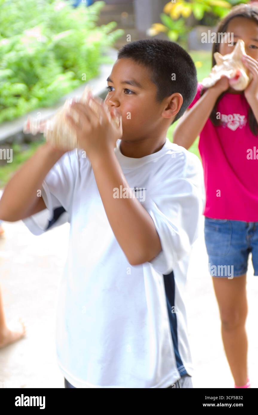 3. Grundschule Schüler hineinblasen Muschelschale als eine uralte Hawaiianische Methode immer Aufmerksamkeit und zu kommunizieren. Stockfoto