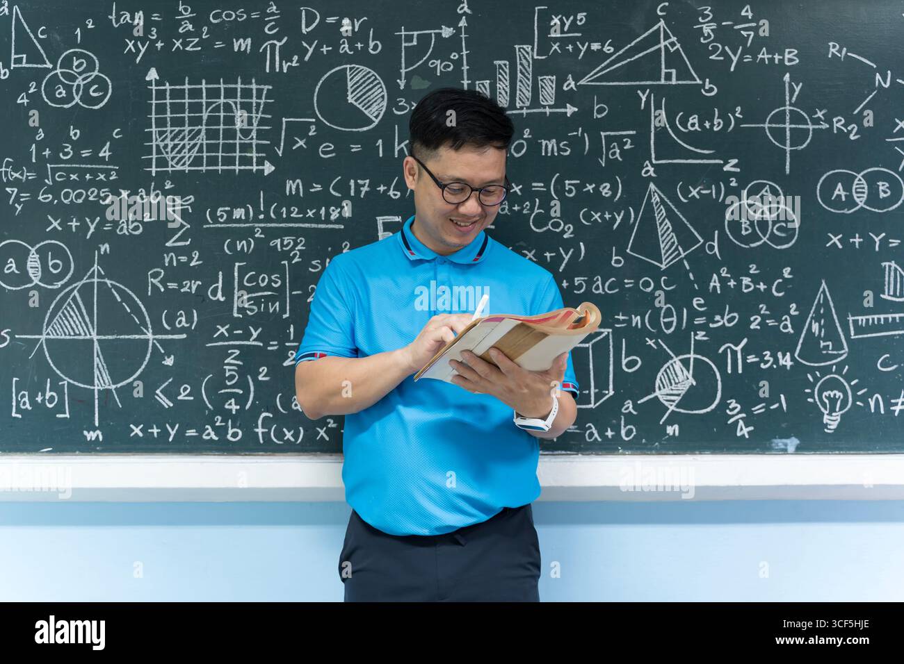 Ein Mathematiklehrer, der ein Buch liest und Notizen schreibt, während er vor einer Tafel steht, die mit Gleichungen gefüllt ist und Bildung, Lernen, aca repräsentiert Stockfoto