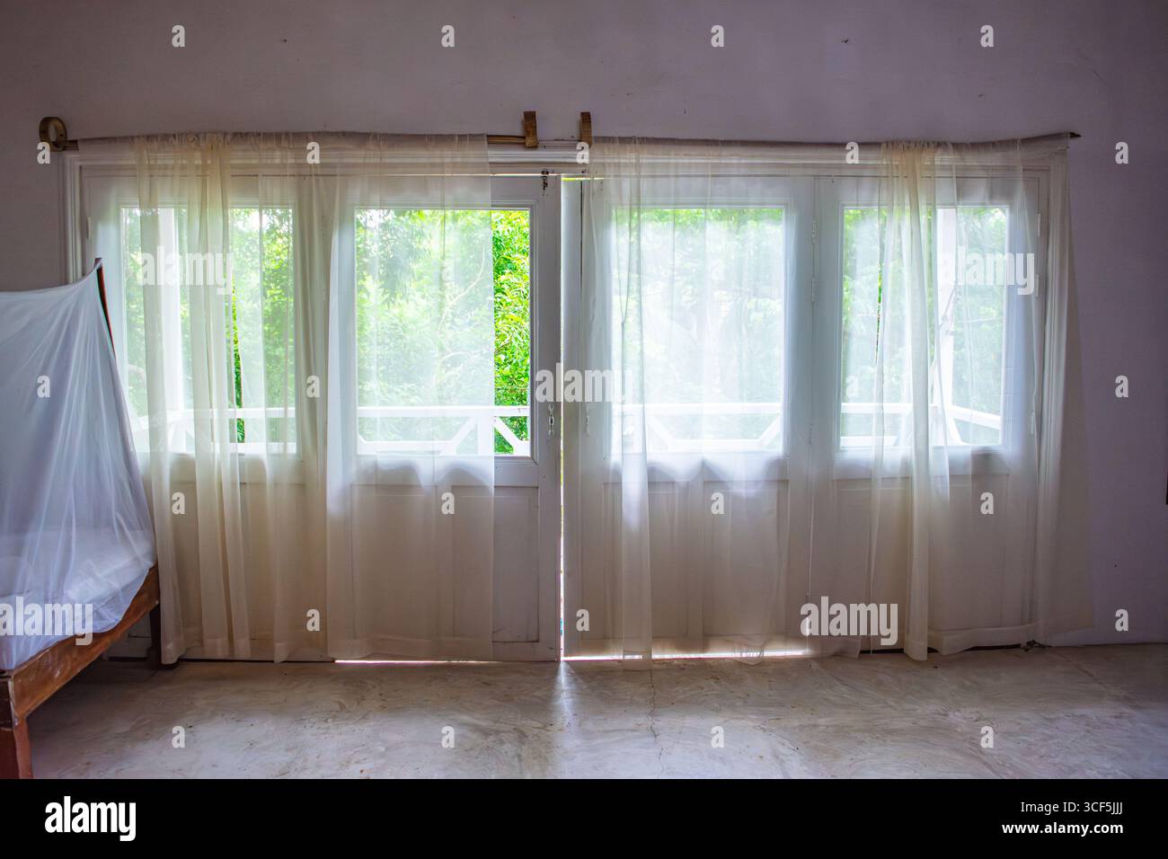 Ein ruhiges Interieur mit transparenten Vorhängen, die einen üppigen grünen Blick auf Rosario Island, Cartagena, Kolumbien, freigeben. Stockfoto