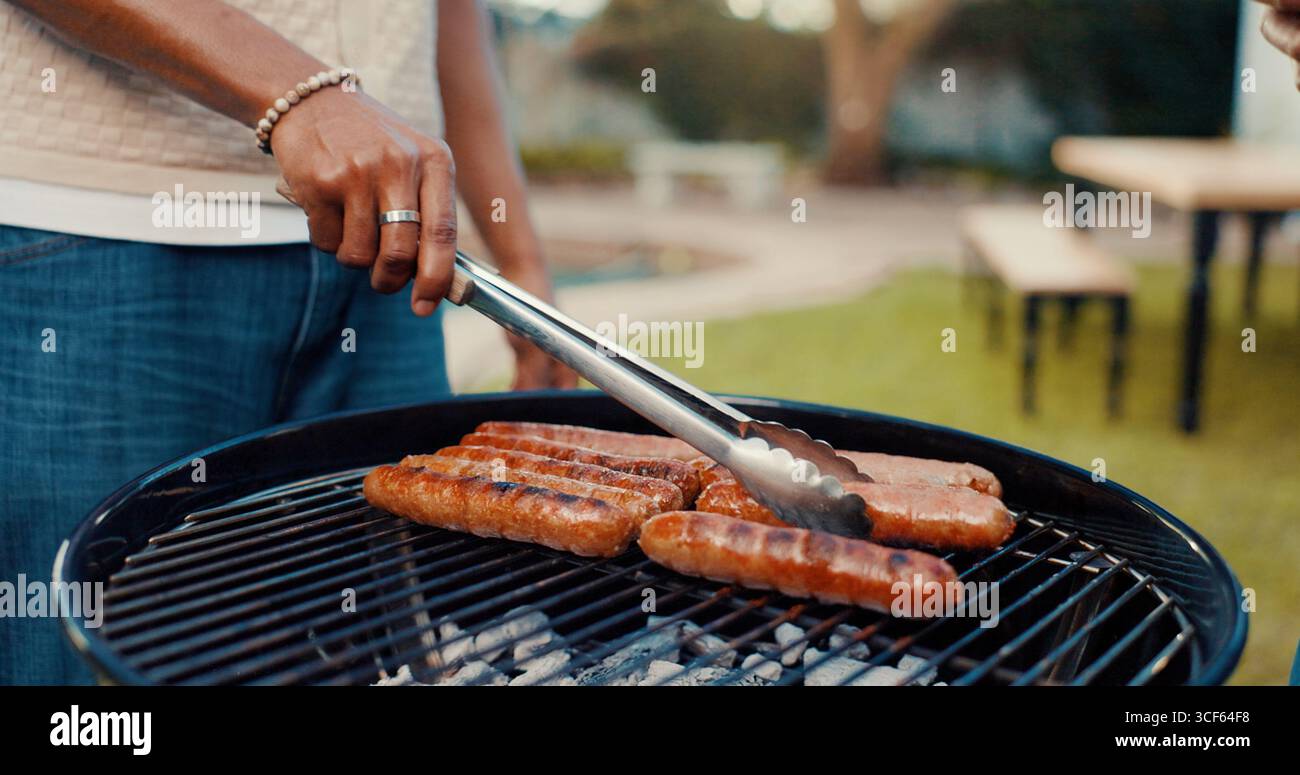 Hände, Person und grillgerichte auf dem Grill zur Zubereitung der Mahlzeiten, gegrillte Würstchen und Kochen für gesellige Zusammenkünfte. Mann, Zange und Grillfleisch auf Hitze zum Mittagessen Stockfoto
