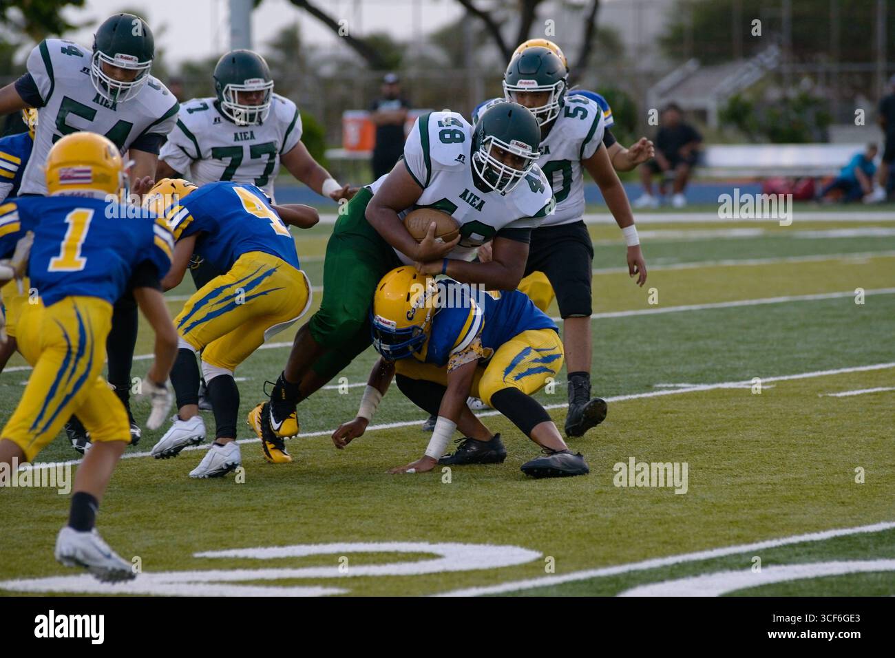 Ein unterdimensionaler High School-Verteidiger taucht ein, um ein Low Tackle gegen ein massives Rücklaufen in vollem Schritt zu spielen – pures Adrenalin und Sand, das auf Gridiron gefroren ist Stockfoto
