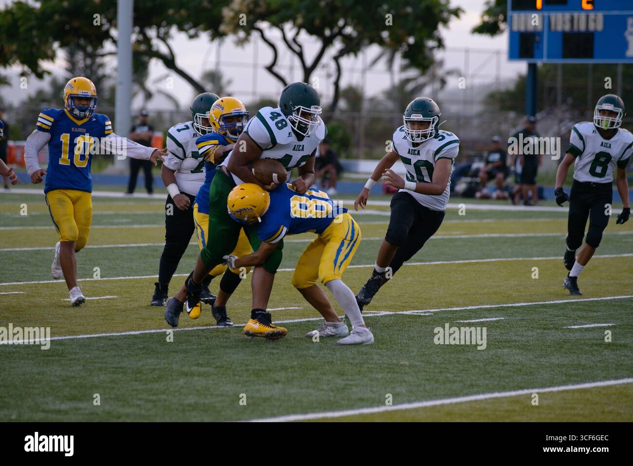 Ein unterdimensionaler High School-Verteidiger taucht ein, um ein Low Tackle gegen ein massives Rücklaufen in vollem Schritt zu spielen – pures Adrenalin und Sand, das auf Gridiron gefroren ist Stockfoto