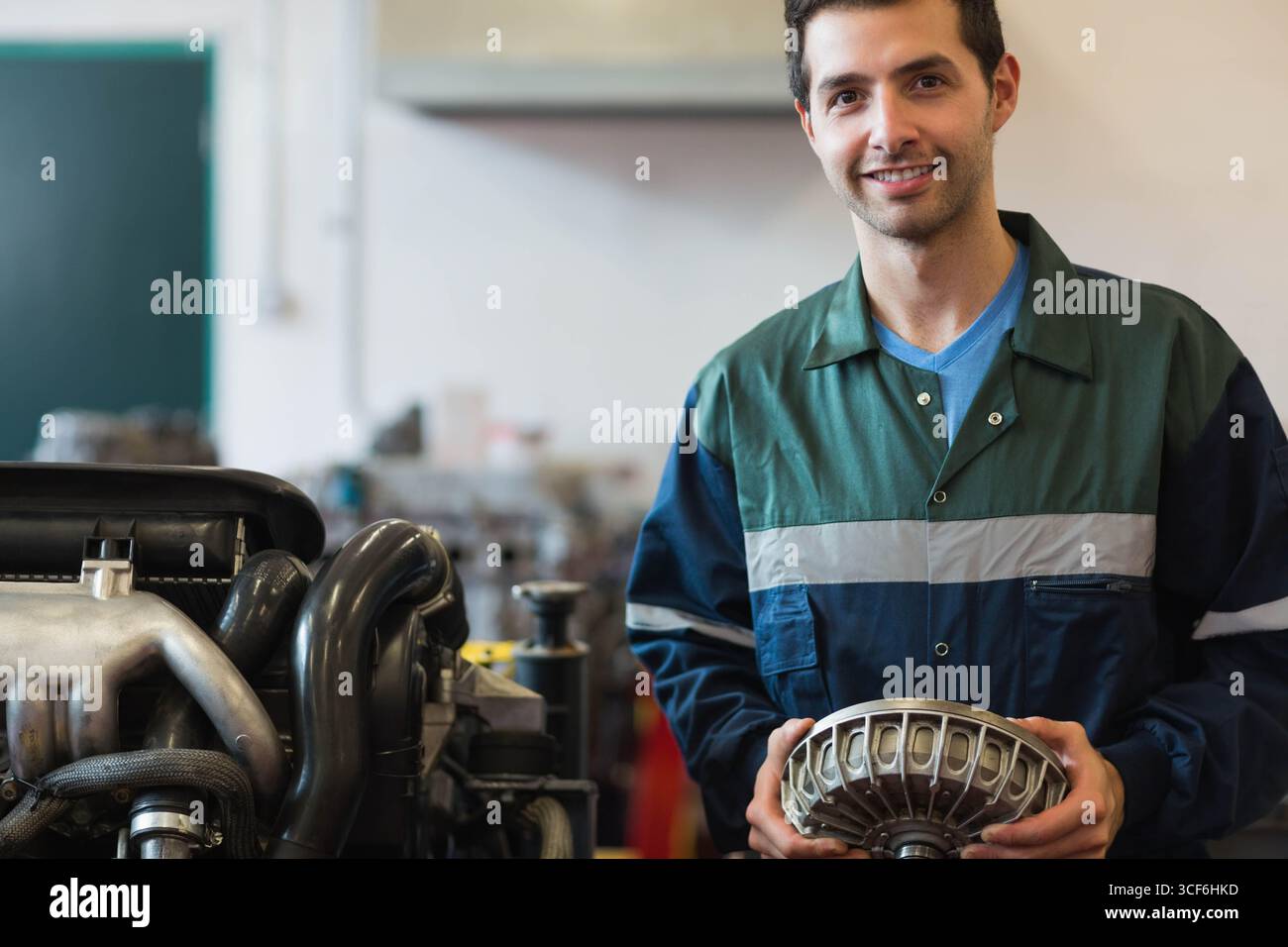 Männlicher Mechaniker mit Overall, der den Konverter neben dem Motorständer in der Werkstatt hält, Kopierraum Stockfoto