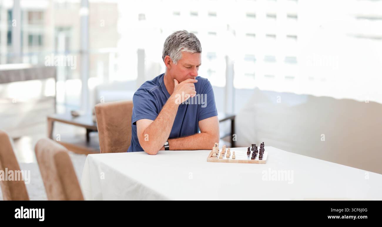 Senior Mann sitzt am Sonnentisch und studiert kleine hölzerne Schachbretter und Schachstücke Stockfoto