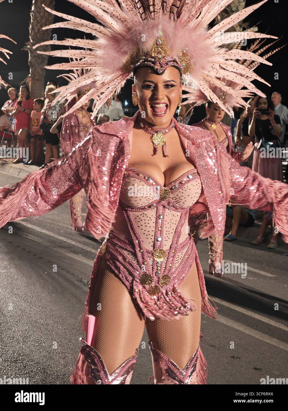 Aguilas, Murcia, Spanien. August 2025. Überschwängliche Tänzerin in Ballkleid und Federn im Haar bei der Sommerparade des Aguilas-Karnevals Stockfoto