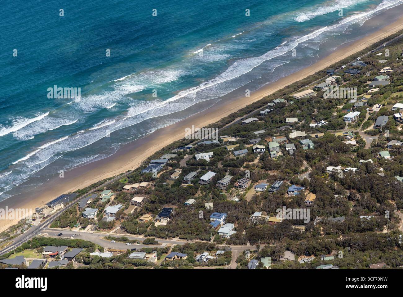 Blick aus der Vogelperspektive auf die Küste, wo das pulsierende türkisfarbene Meer auf den Sandstrand trifft, im Kontrast zur üppigen grünen Vegetation und verstreuten Häusern, Anglesea, Victoria, Australien. Stockfoto
