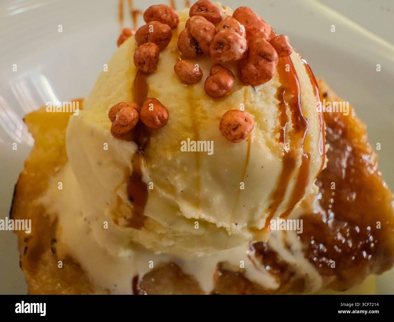 Nahaufnahme eines Pfirsichschuhs mit Vanilleeis, Karamellsauce und knusprigen Toppings, die einen verlockenden Sommergenuss schaffen Stockfoto