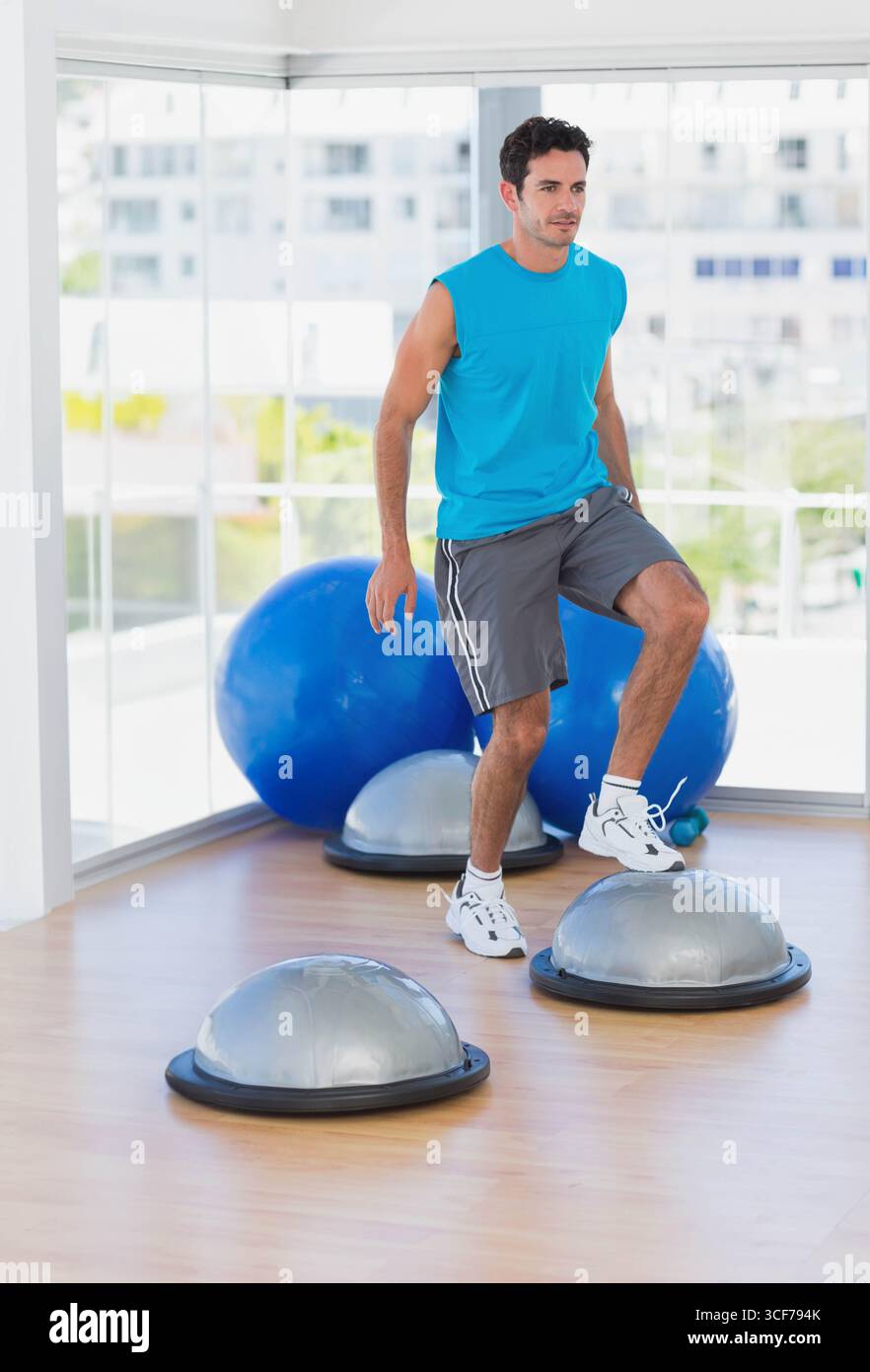 Männlich in den frühen 30er Jahren, balanciert auf einem Halbkuppeltrainer mit Übungsbälle auf dem Studioboden, Kopierraum Stockfoto