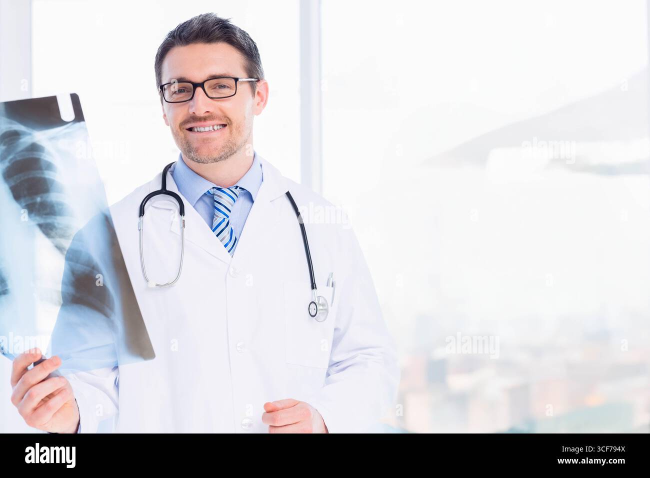 Männlicher Arzt, der den Thoraxröntgenfilm am Fenster in der Klinik mit Laborkittel und Stethoskop überprüft Stockfoto