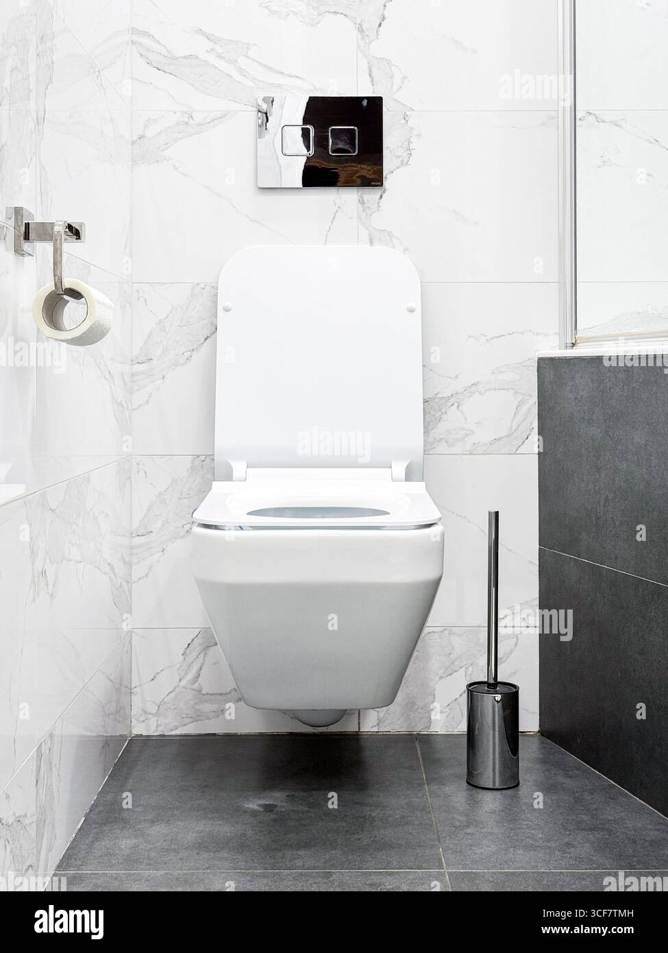 Moderne Toilettenschüssel mit eingebautem Wassertanksystem. Weiße Marmorfliesen an den Wänden und moderner grauer Boden. Stockfoto