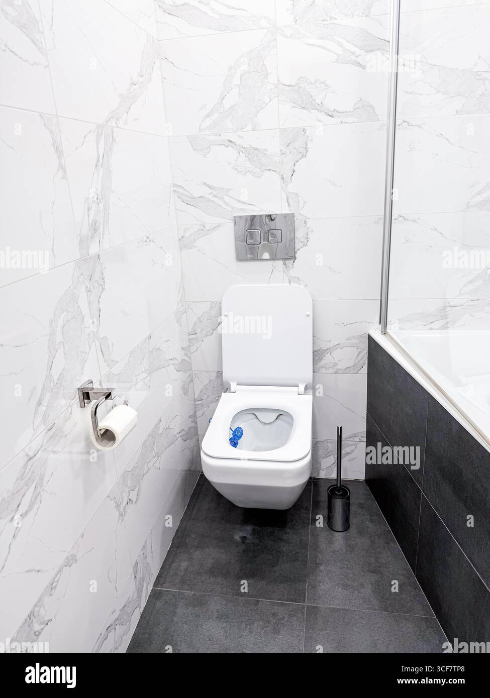 Moderne Toilettenschüssel mit eingebautem Wassertanksystem. Weiße Marmorfliesen an den Wänden und moderner grauer Boden. Stockfoto