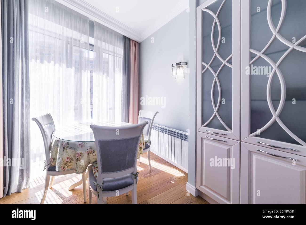 Ein weißer Esstisch mit einer Tischdecke mit Blumenmuster und vier Stühlen. Das Zimmer ist gut beleuchtet und hat ein sauberes, modernes Aussehen Stockfoto