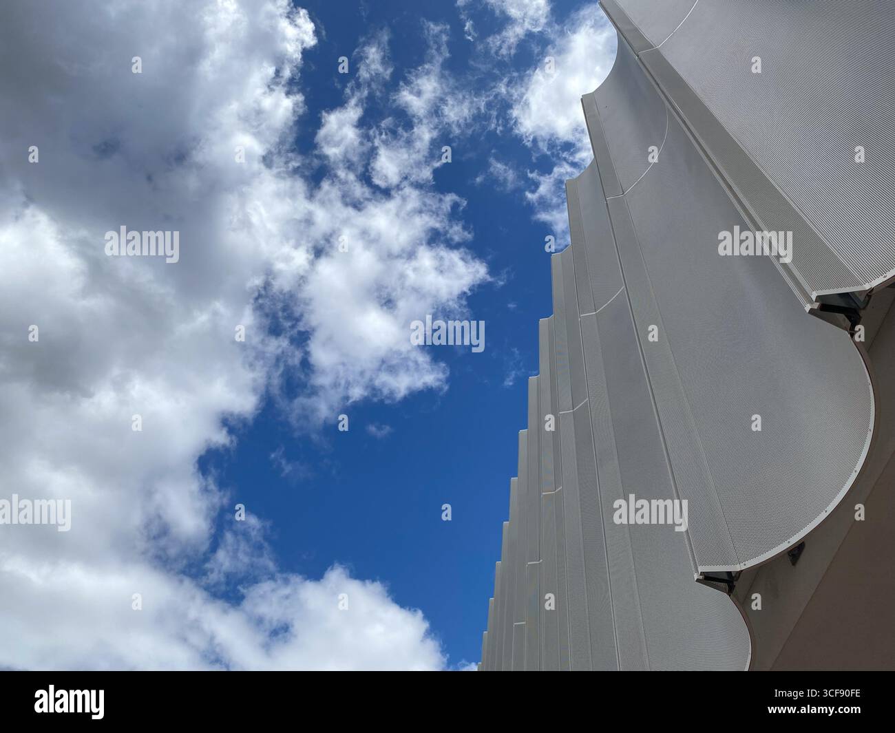 Flacher architektonischer Blick mit gewellten Metallpaneelen des zeitgenössischen Gebäudes vor dem wolkenblauen Himmel in Pescara, Italien Stockfoto