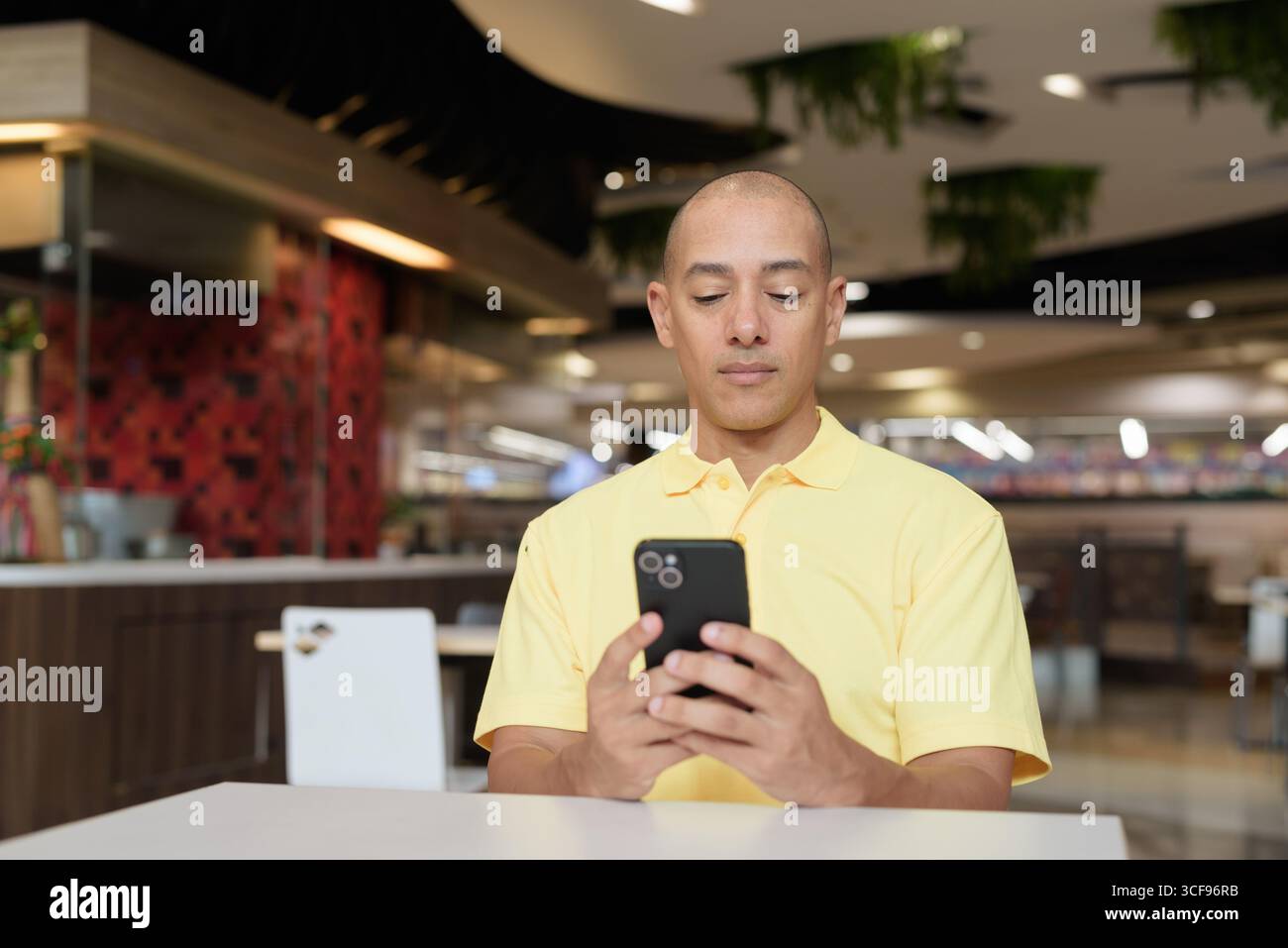 Porträt eines Reifen italienischen Mannes, der drinnen in einem modernen Restaurant sitzt und das Telefon aus der Ferne arbeitet Stockfoto