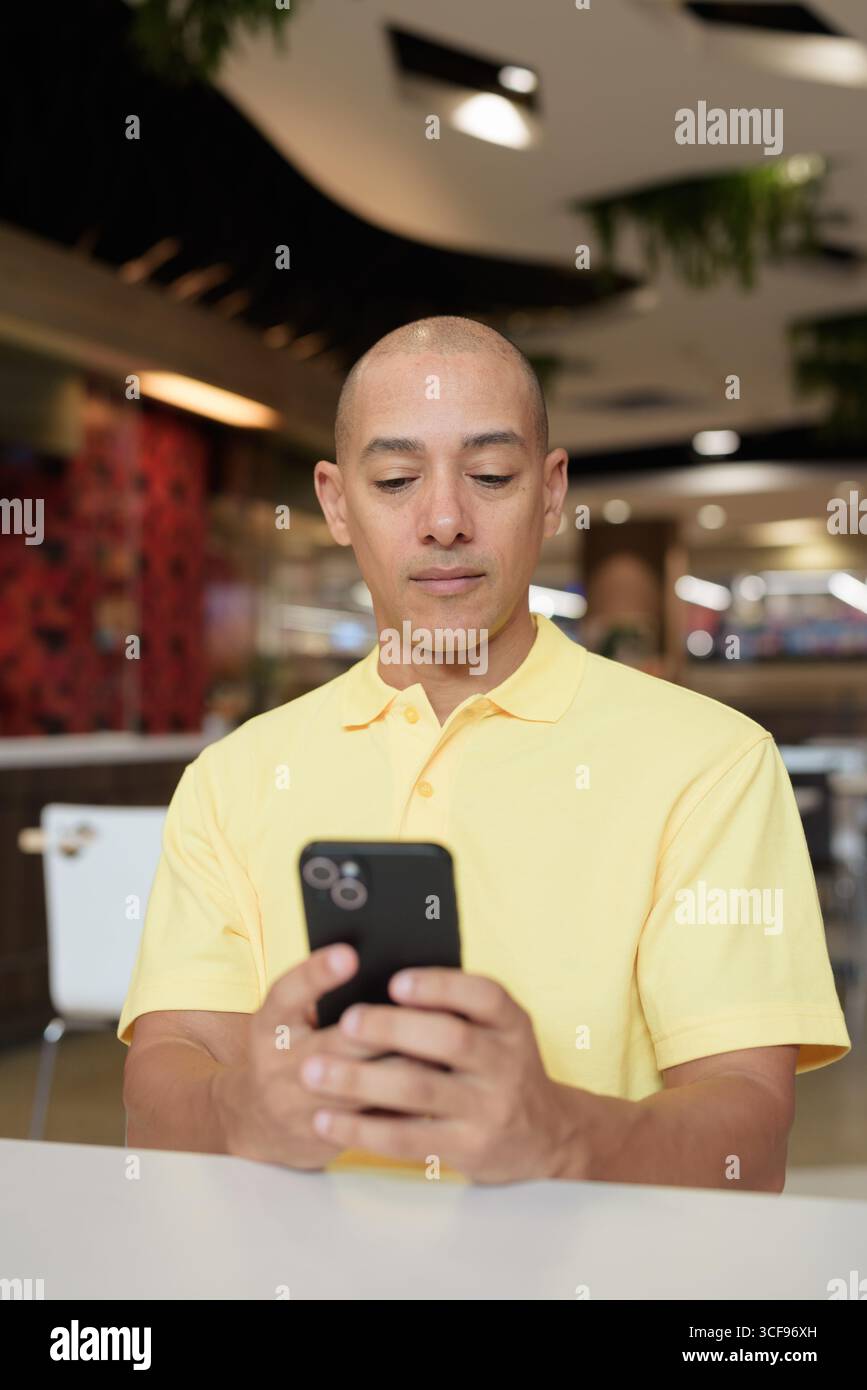 Porträt eines Reifen italienischen Mannes, der drinnen in einem modernen Restaurant sitzt und das Telefon aus der Ferne arbeitet Stockfoto