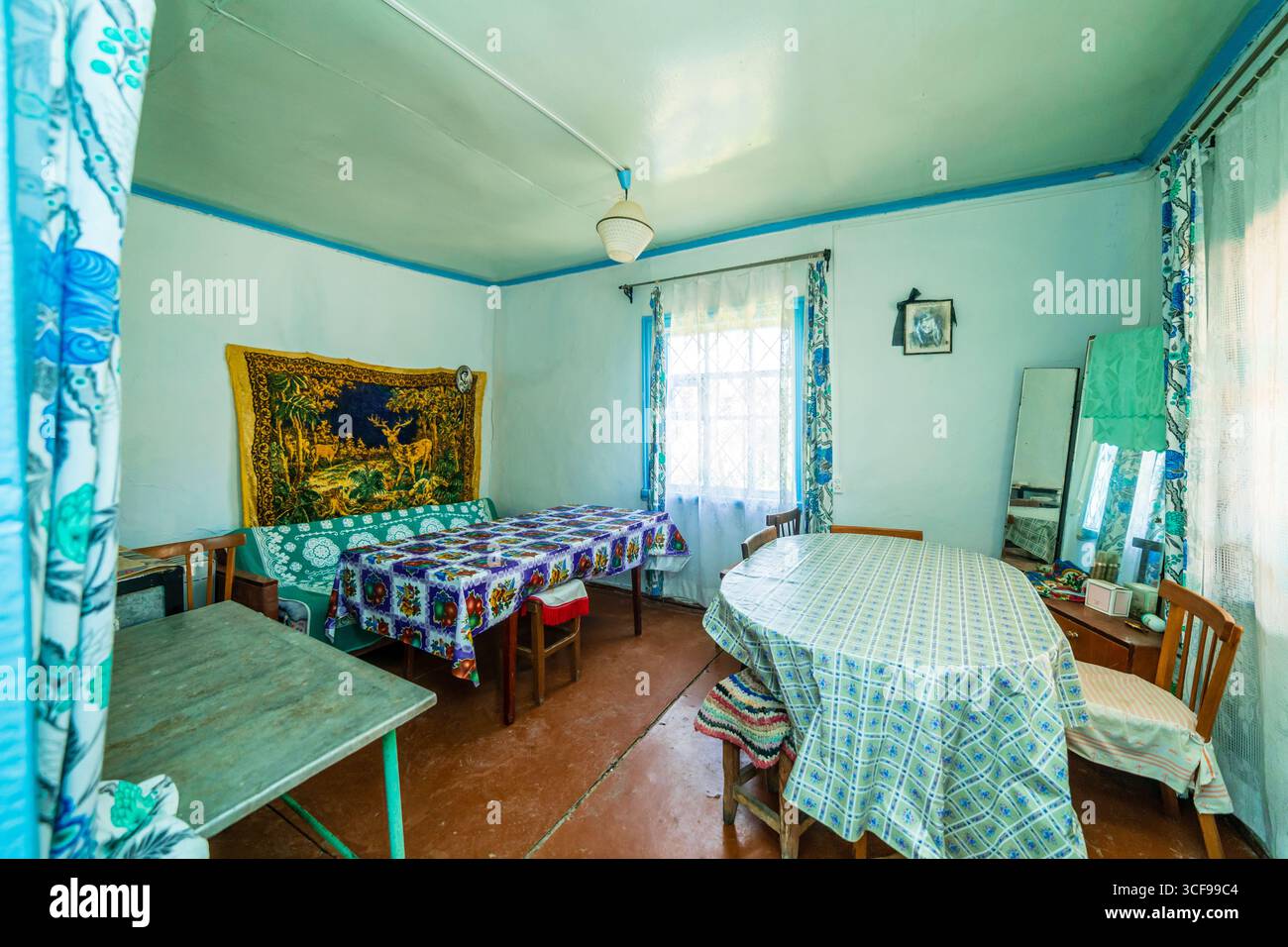 Ein Zimmer in einem baufälligen Landhaus. Grünliche Wände, alte Möbel, Öltuch auf dem Tisch. Teppich und alte Fotos an der Wand. Stockfoto