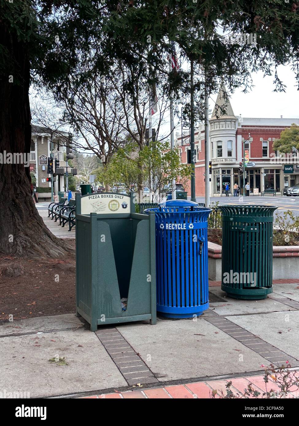 Öffentliche Recycling- und Abfallbehälter, einschließlich eines Behälters, der nur für Pizzakästen verwendet wird, befinden sich in einem Stadtteil mit historischen Gebäuden und Geschäften - Smartphone-aufgenommenes Stockfoto