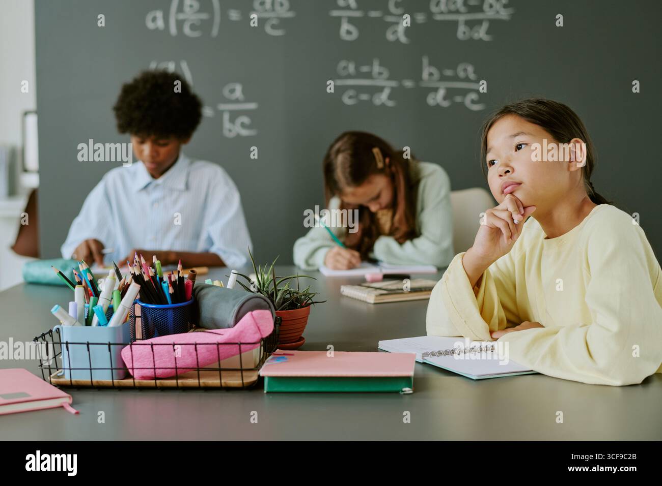 Asiatisches Mädchen denkt, während es mit verschiedenen Teenagern im Klassenzimmer sitzt Stockfoto