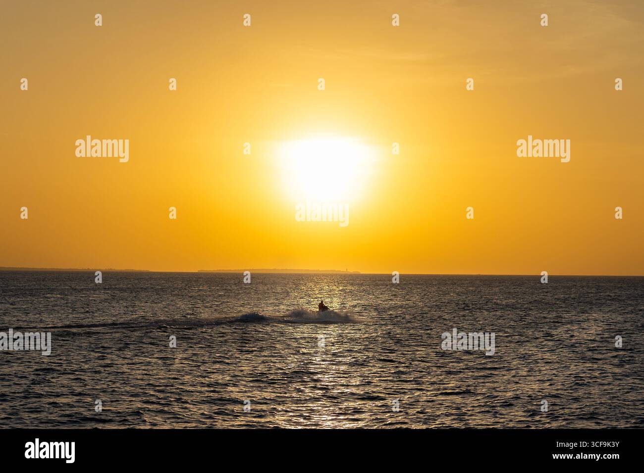Goldener Sonnenuntergang von Sansibar mit einem Jetski, der über das glühende Wasser gleitet. Stockfoto