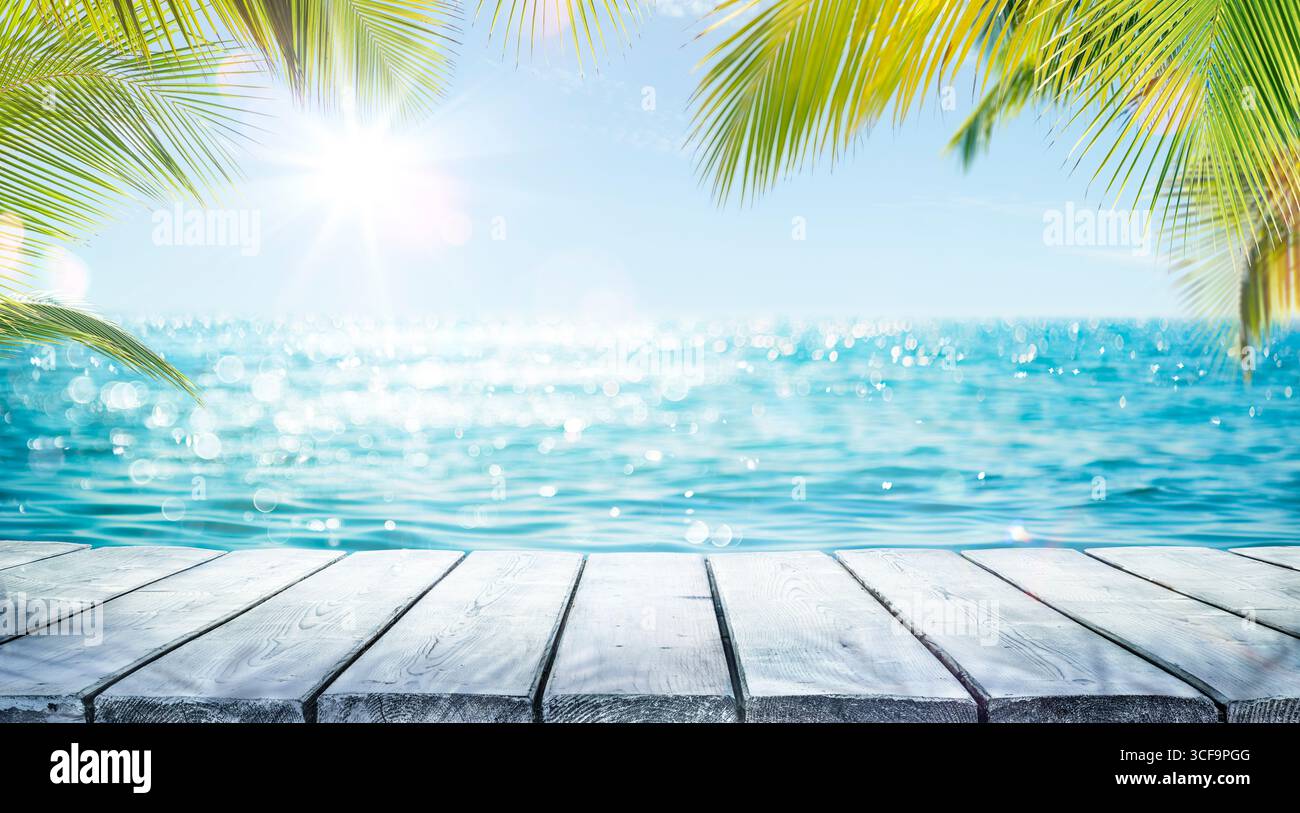 Tropischer Sommertisch - Meer Und Leerer Holztisch Mit Palmblättern - Flare-Effekt Und Abstraktes Bokeh-Licht Im Unscharfen Ozean Stockfoto