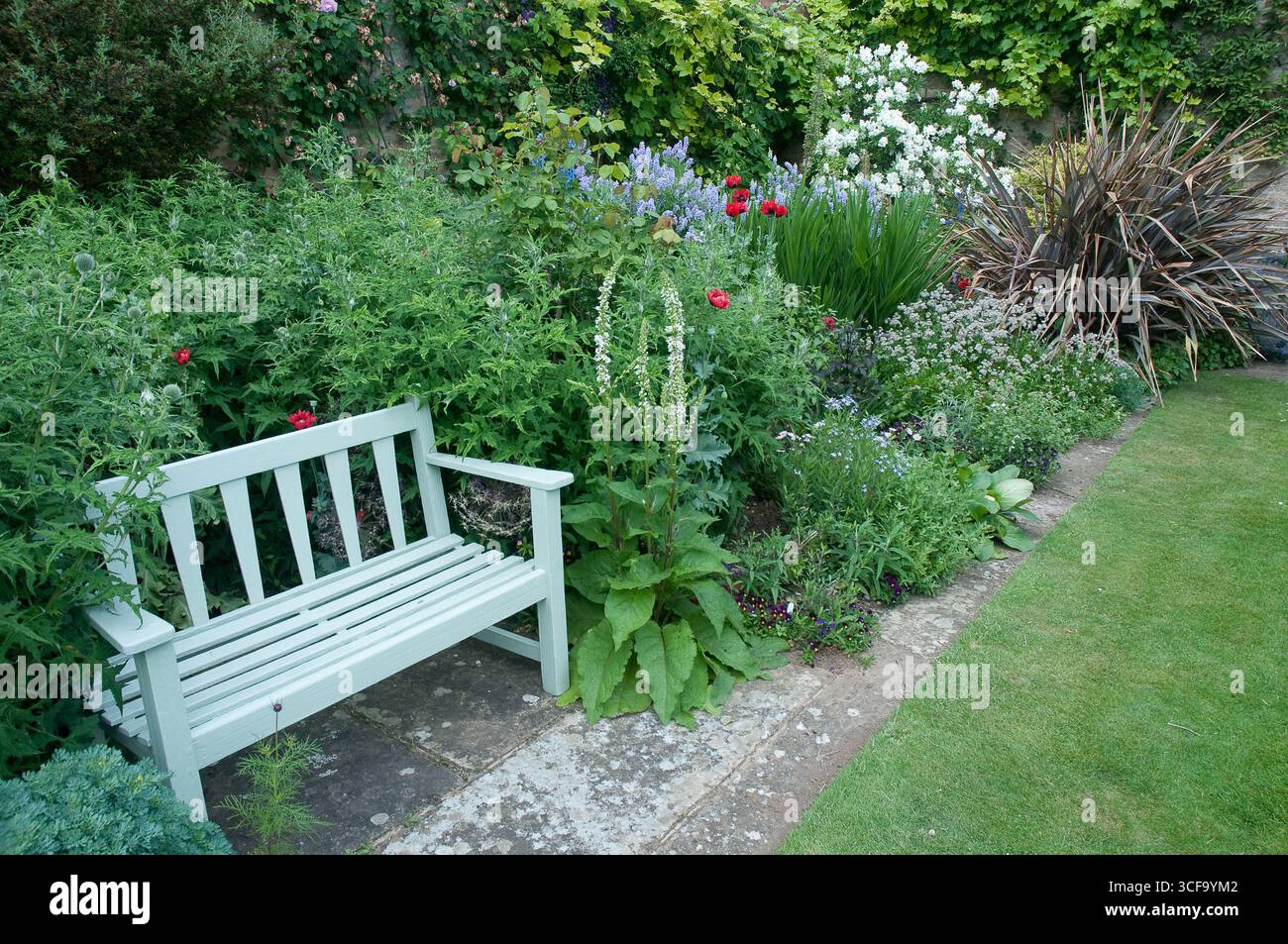 Üppiges Grün umgibt eine rustikale Bank inmitten eines pulsierenden Blumengartens und schafft einen friedlichen Rückzugsort voller farbenfroher Blüten. Stockfoto