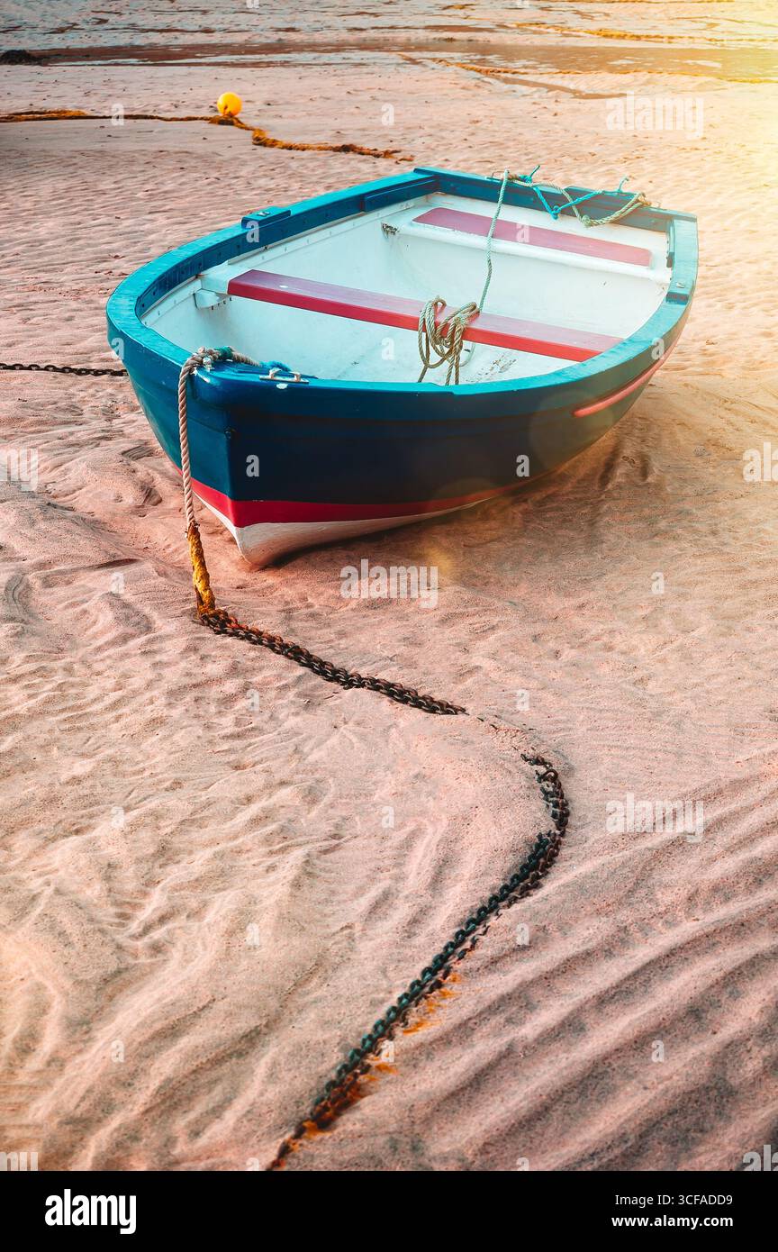 Ein kleines Boot liegt an einem Sandstrand, der von einer Kette befestigt ist. Ruhige Küstenszene im Retro-Filmstil Stockfoto