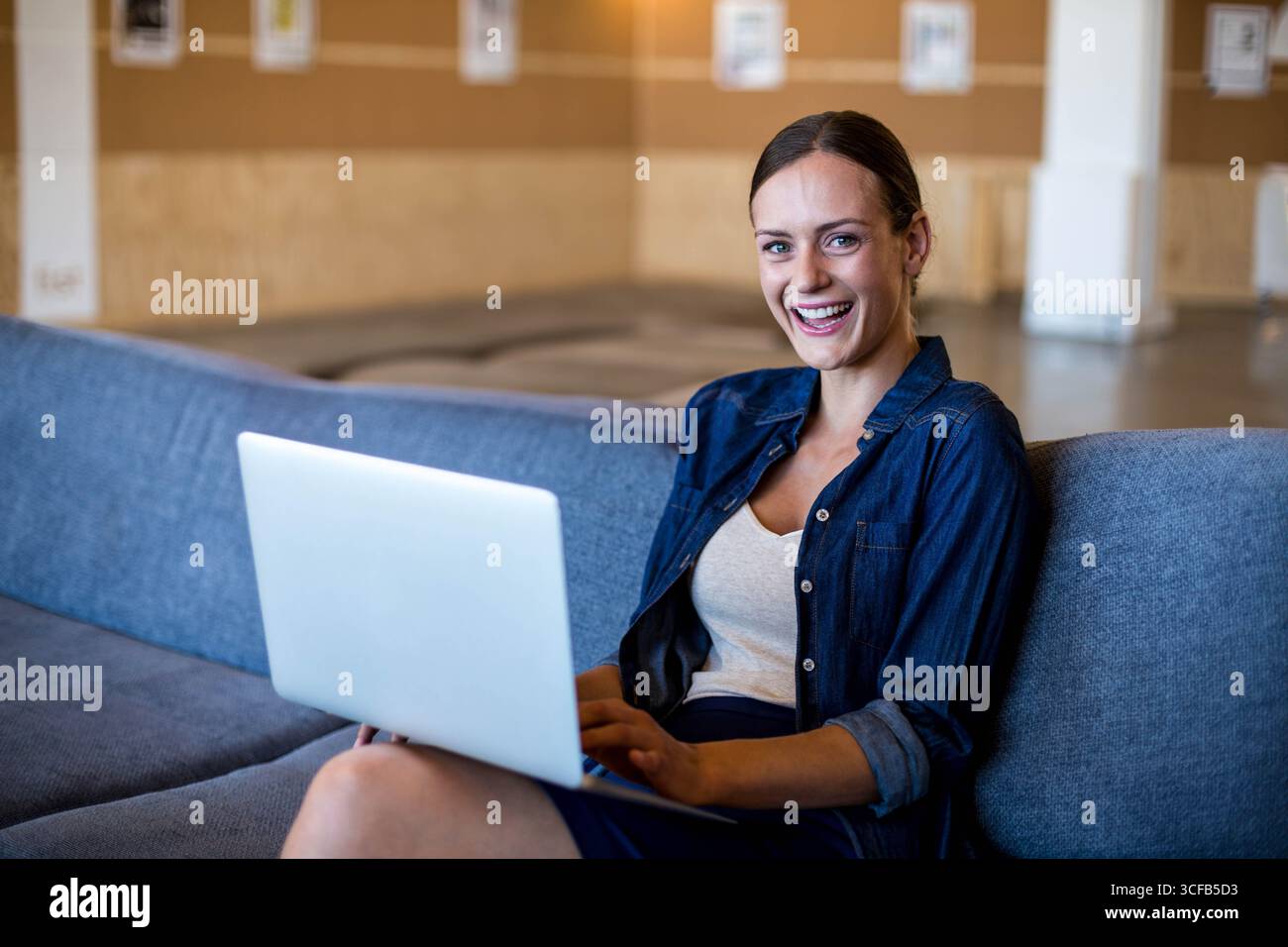 Laptop auf dunkelgrauem Sofa in der modernen Bürolounge mit Kork-Pinnwand Stockfoto