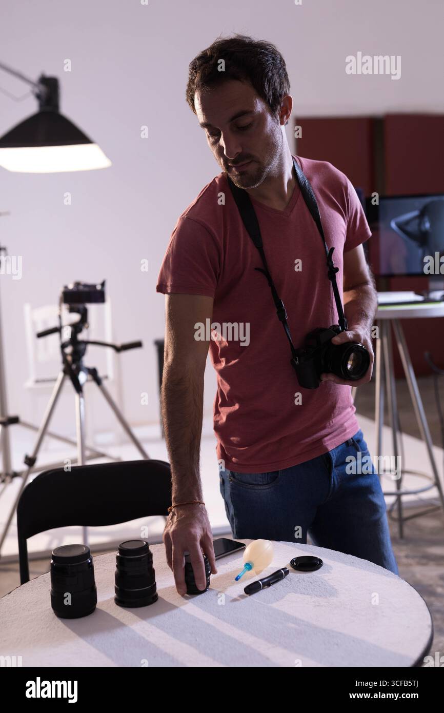 Mittelgroßer Mann, der im Studio neben dem Tisch steht und die DSLR-Kamera und Objektive für Studioaufnahmen organisiert Stockfoto