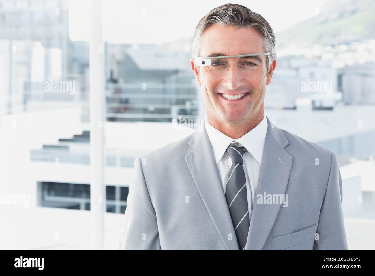 Geschäftsmann lächelt vor dem raumhohen Fenster, trägt Anzug und intelligente Brille, Kopierraum Stockfoto
