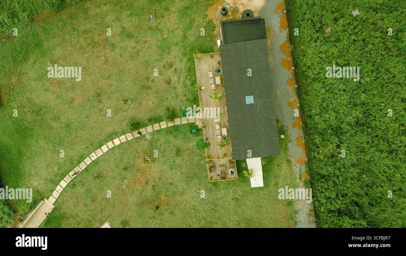 Blick aus der Vogelperspektive auf ein Gebäude mit dunklem Dach, umgeben von grünem Gras und Steinweg, bietet einen starken Kontrast von natürlichen und architektonischen Elementen, Epe, Lagos, Nigeria. Stockfoto