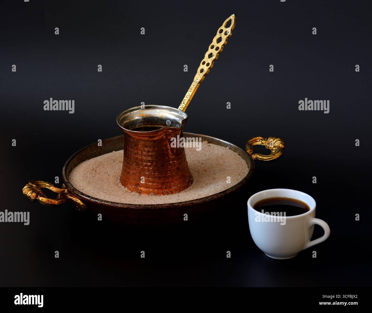 Kupfertürke in einem Tablett mit Sand und einer Tasse heißem frisch gebrühtem schwarzem Kaffee auf schwarzem Hintergrund. Nahaufnahme. Stockfoto