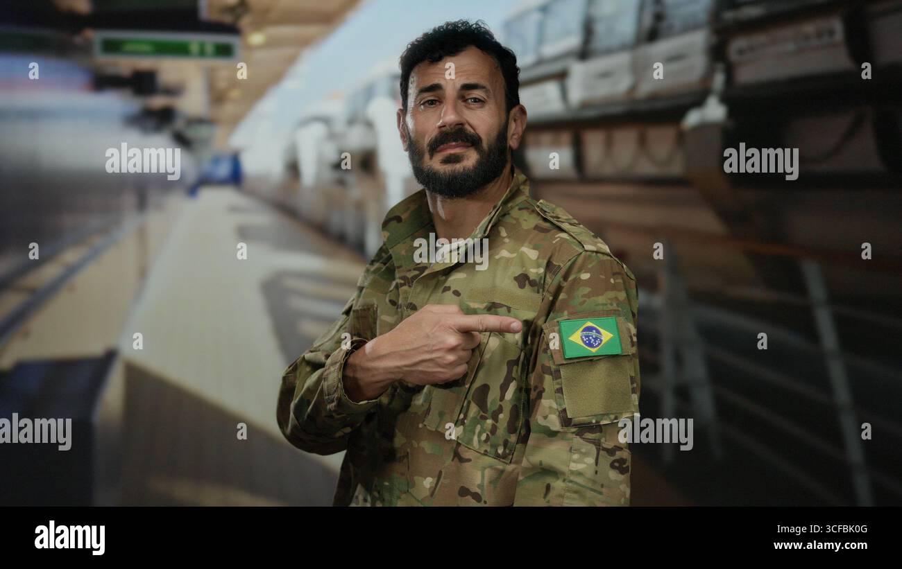 Mann in Militäruniform mit brasilianischem Flaggenaufnäher auf der Schulter steht auf dem Deck des Kreuzfahrtschiffes und zeigt selbstbewusst unter hellem Licht auf die Flagge. Stockfoto