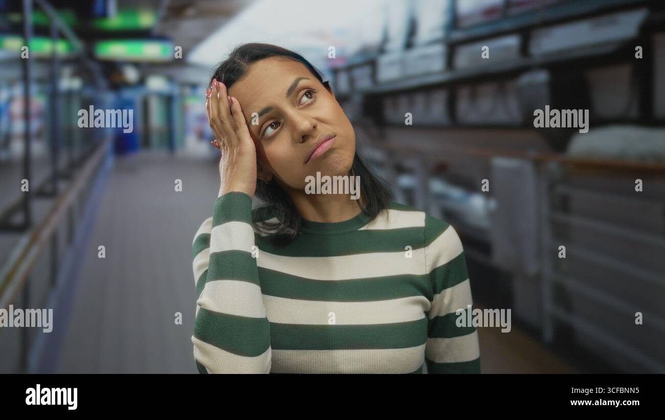 Frau mit gestreiftem Pullover auf Kreuzfahrtschiff mit einem nachdenklichen Ausdruck, während die Meeresbrise sanft durch das Außendeck zieht und eine ruhige Atmosphäre schafft Stockfoto