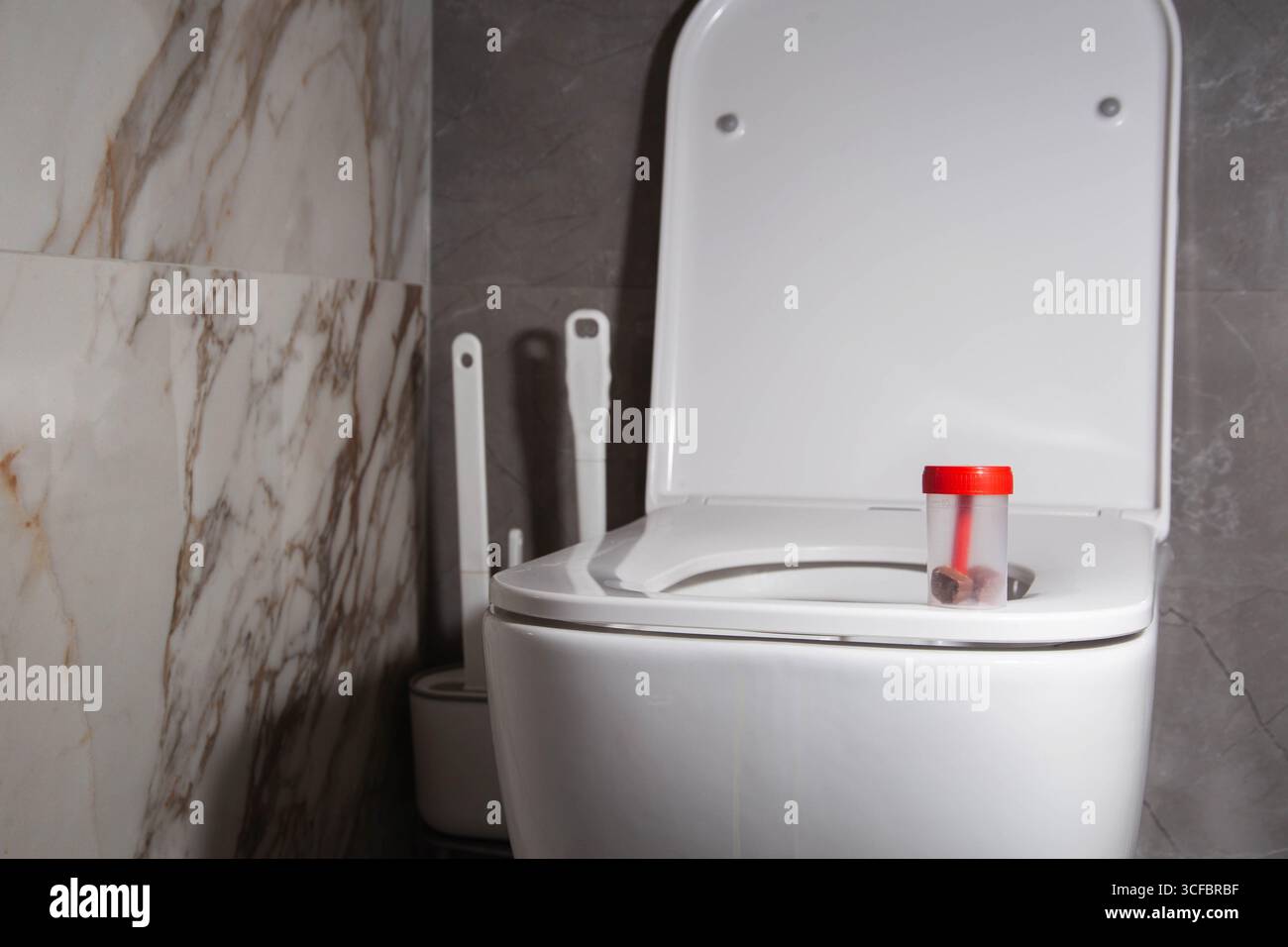 Steriler Behälter mit Stuhltest auf der Toilettenschüssel in der Toilette. Das Konzept der Stuhluntersuchung auf Eierwurm und Koprogramm. Kopierbereich für Text Stockfoto