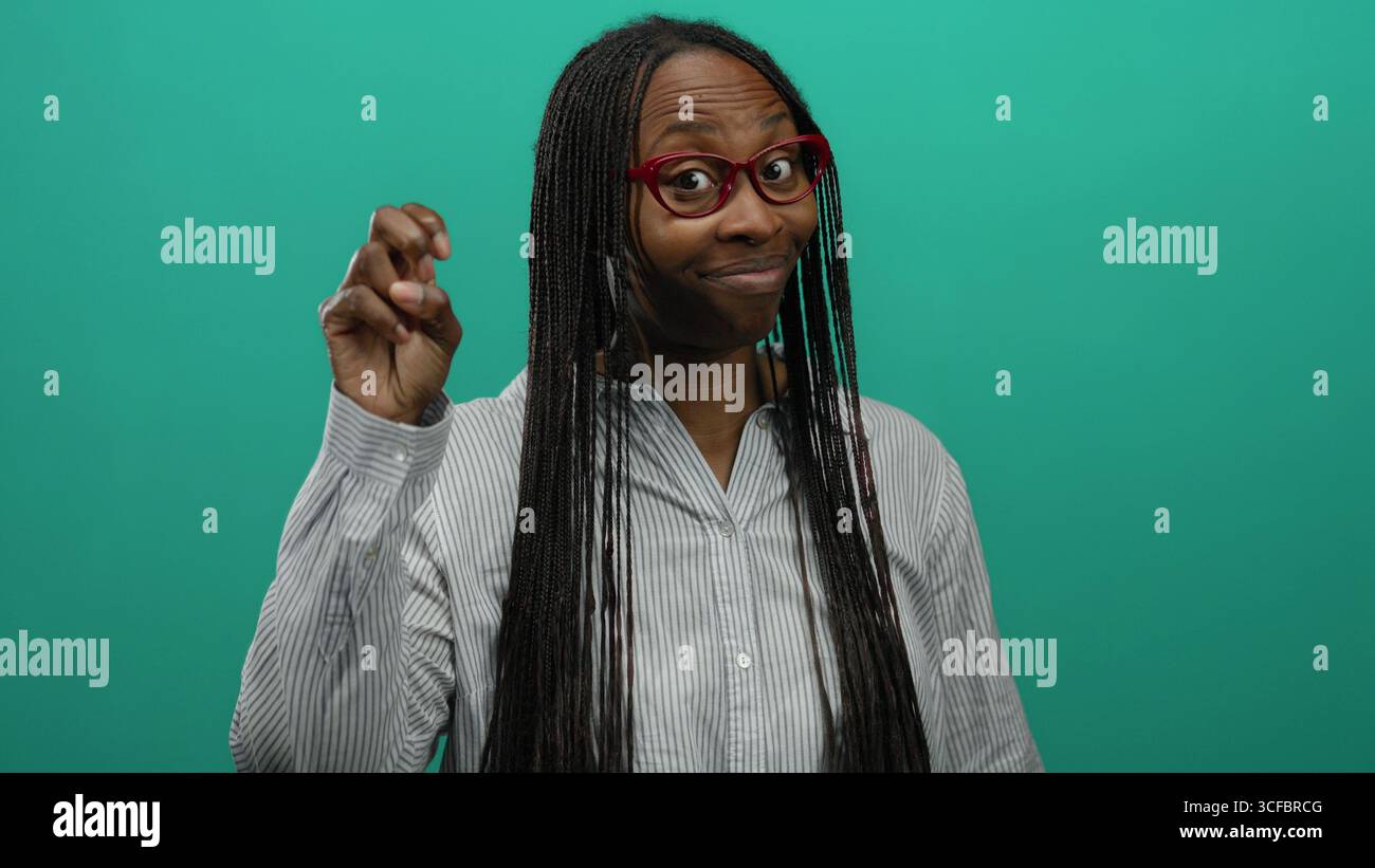 Frau mit langen Haaren und einer Brille, die Zitate vor grünem Hintergrund macht, gestreiftes Hemd trägt, Selbstvertrauen und Humor ausstrahlt. Stockfoto