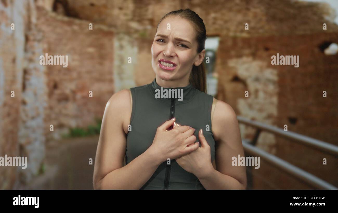 Eine grimmige junge kaukasische Frau, die die Brust an verwitterten antiken römischen Ruinen hält; Herzanfall-Schmerz. Stockfoto