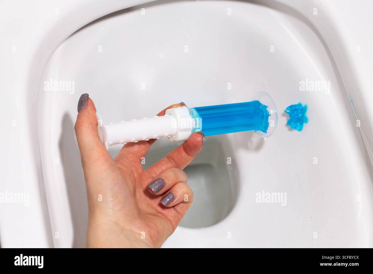 Eine Spritze mit ozeanduftendem Gel zur Reinigung und Desinfektion der Toilette in einer Hand vor dem Hintergrund einer Toilette. Antibakterielle Wirkung Stockfoto