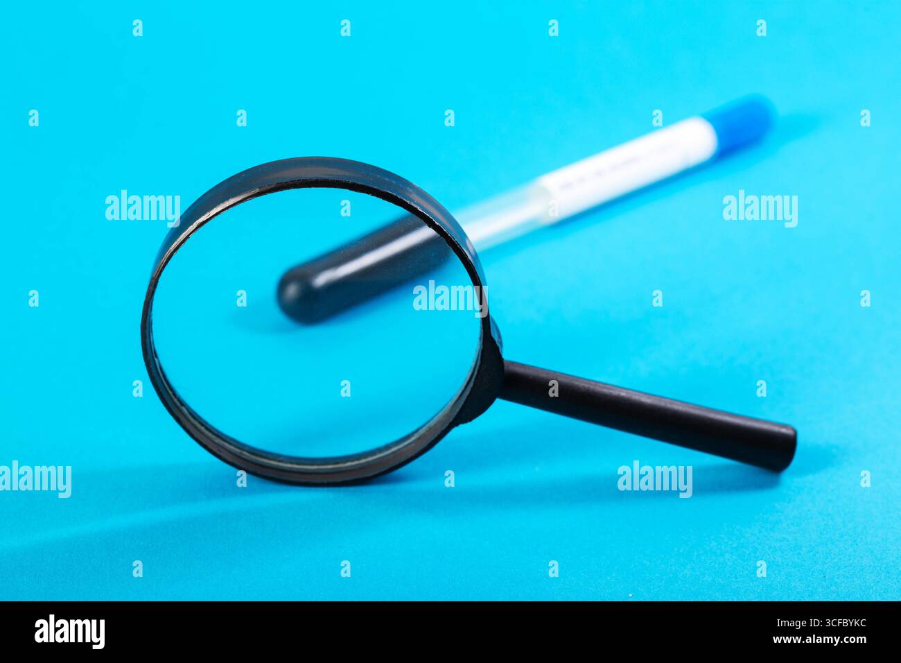 Eine Lupe vor dem Hintergrund eines sterilen Reagenzglases mit Vitaminanalyse und blauem Hintergrund. Analyse eines Vitami-Komplexes Stockfoto